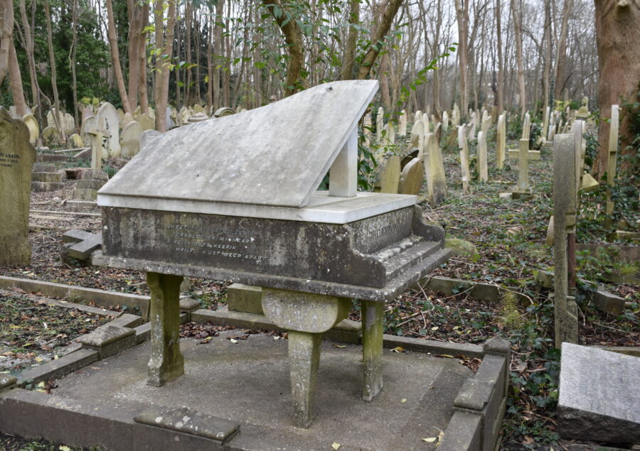 Unique gravestone shaped like a piano, located in a tranquil cemetery surrounded by trees. A poignant reminder of music and memory.
