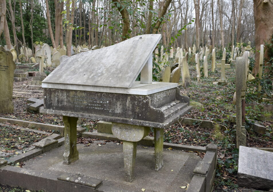 Unique gravestone shaped like a piano, located in a tranquil cemetery surrounded by trees. A poignant reminder of music and memory.